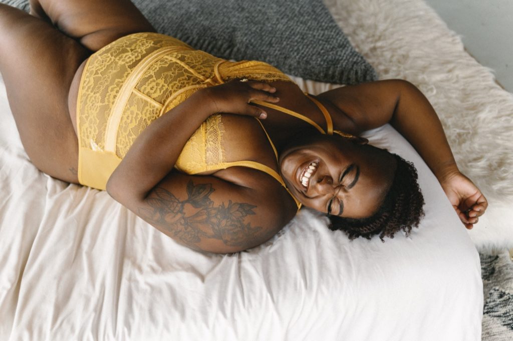 Individual boudoir session, laughing and laying on bed in yellow bodysuit