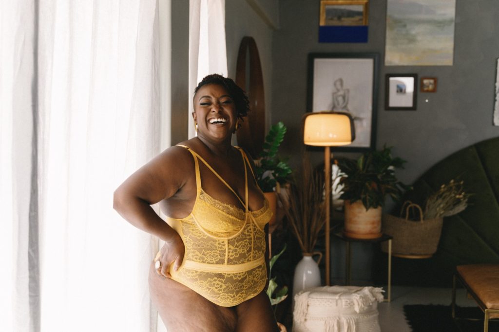Individual boudoir session in strappy yellow bodysuit, standing in studio, laughing