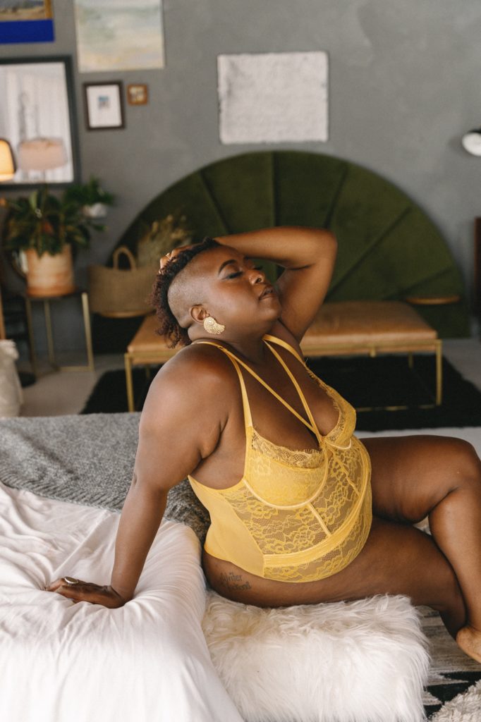 Individual boudoir session in strappy yellow bodysuit, sitting on bed