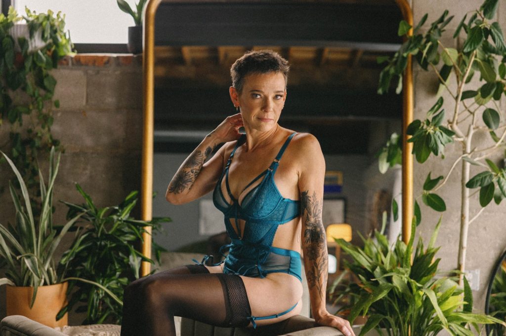 Individual boudoir photos, woman in blue bodysuit posing in front of mirror with plants
