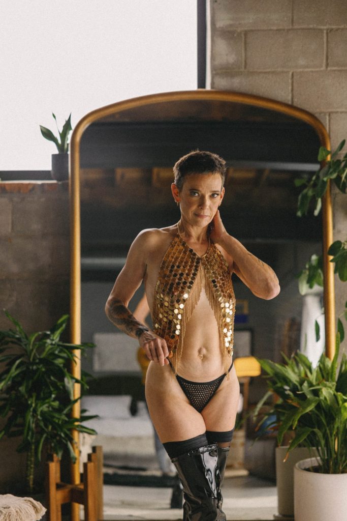 Individual boudoir photos, woman in gold sequin top, thong, and black leather boots in front of mirror and plants
